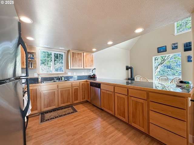 kitchen with kitchen peninsula, appliances with stainless steel finishes, sink, light wood-type flooring, and a textured ceiling