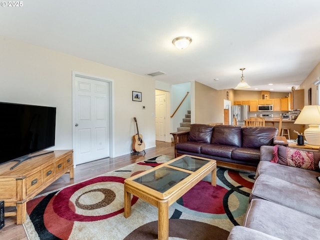 living area with stairs, visible vents, and light wood-style floors