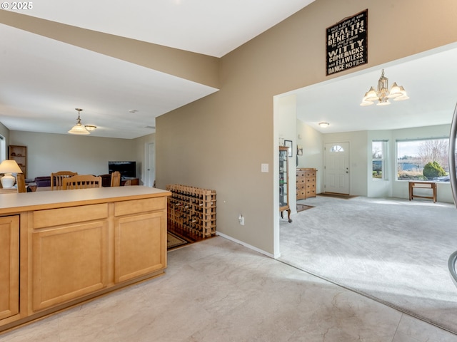 kitchen featuring baseboards, light colored carpet, open floor plan, pendant lighting, and a notable chandelier