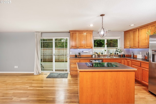 kitchen with stainless steel fridge, light wood-style flooring, a kitchen island, decorative light fixtures, and a sink