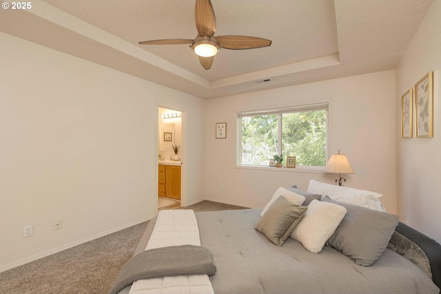 bedroom with a tray ceiling, light colored carpet, baseboards, and ensuite bath