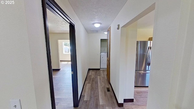 132 NE Rifle Range St, Roseburg, OR 97470 - hall featuring washing machine and clothes dryer, a textured ceiling, wood finished floors, and baseboards