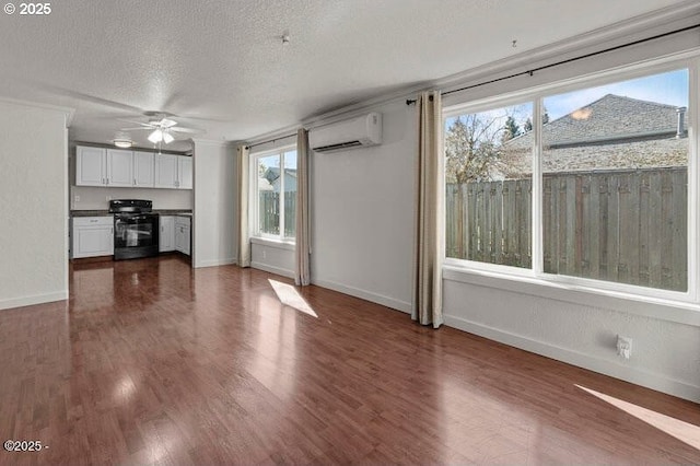 unfurnished living room featuring a wall mounted AC, ceiling fan, a textured ceiling, healthy amount of natural light, and baseboards