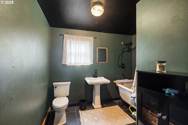 bathroom featuring toilet, a sink, a tub, tile patterned flooring, and baseboards