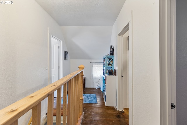 hallway with a textured ceiling, a textured wall, an upstairs landing, vaulted ceiling, and dark wood-style floors