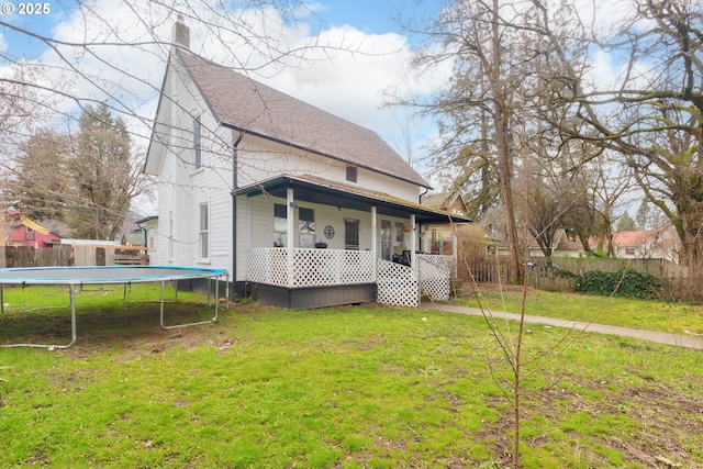 back of house featuring a shingled roof, a lawn, a trampoline, fence, and a porch