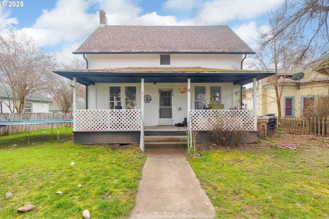 view of front facade featuring covered porch, a front lawn, a chimney, and a shingled roof