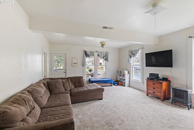 carpeted living room featuring visible vents, beamed ceiling, and a wood stove