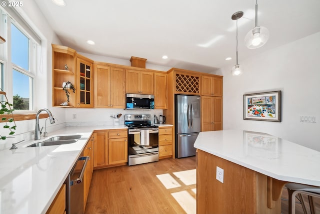 kitchen featuring light countertops, a sink, glass insert cabinets, stainless steel appliances, and light wood-style floors