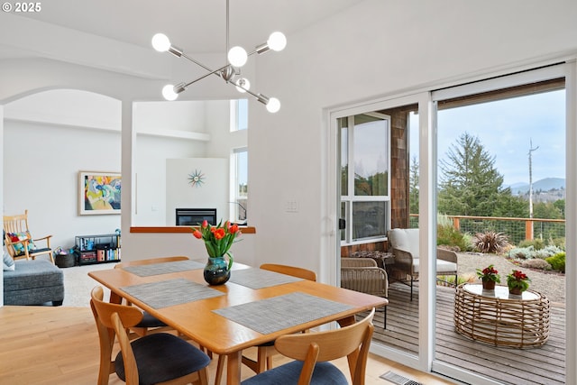 dining area with light wood finished floors, visible vents, a glass covered fireplace, and a healthy amount of sunlight