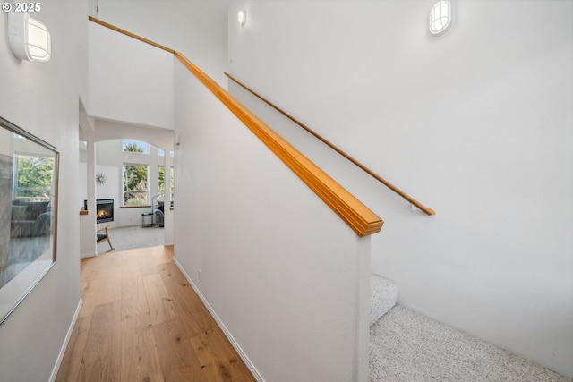staircase with a high ceiling, a glass covered fireplace, and wood finished floors