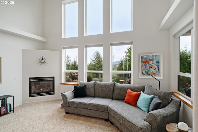 living area with carpet floors, a glass covered fireplace, a towering ceiling, and a wealth of natural light