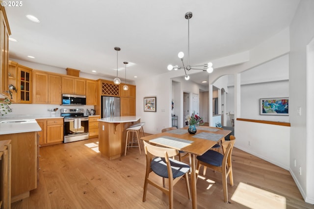 dining area with a notable chandelier, light wood finished floors, baseboards, arched walkways, and recessed lighting