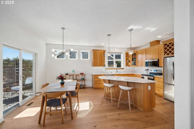 kitchen with light countertops, a sink, a kitchen island, appliances with stainless steel finishes, and light wood-style floors