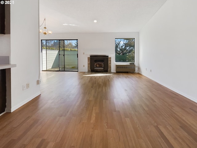 unfurnished living room with a notable chandelier, wood finished floors, radiator, a fireplace, and baseboards