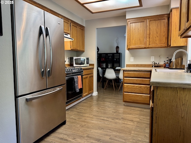 24035 SW Mountain Creek Rd, Sherwood, OR 97140 - kitchen featuring stainless steel appliances, a sink, light wood finished floors, under cabinet range hood, and brown cabinetry