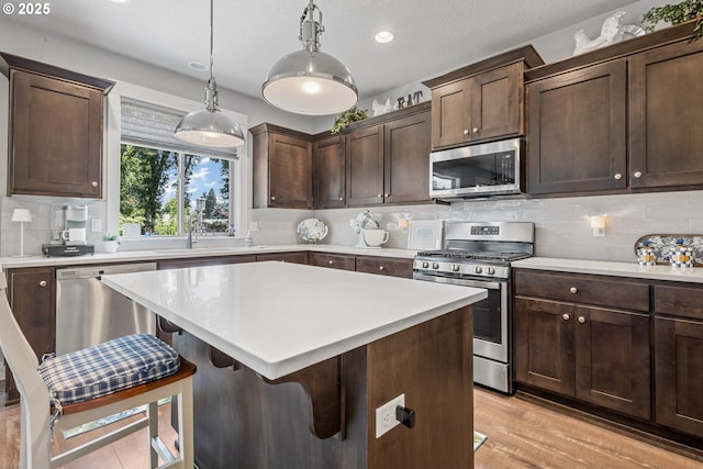 52152 Casswell Dr, Scappoose, OR 97056 - kitchen featuring appliances with stainless steel finishes, light countertops, a breakfast bar, dark brown cabinetry, and decorative backsplash