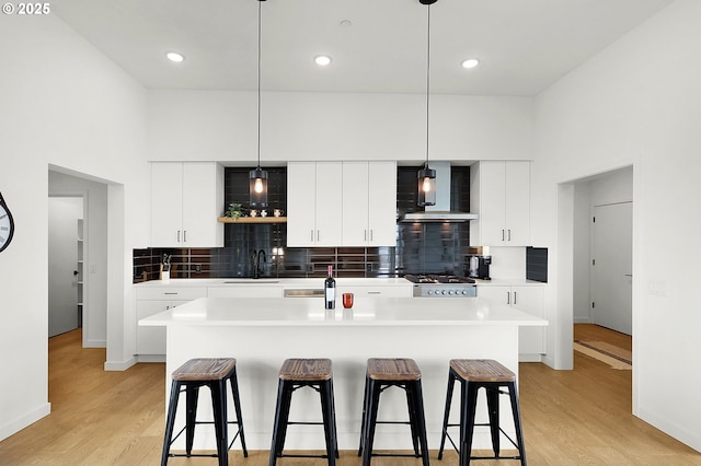 kitchen with light hardwood / wood-style floors, white cabinetry, wall chimney exhaust hood, and an island with sink