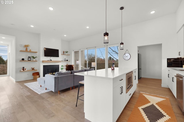 kitchen with a center island, a tile fireplace, white cabinets, hanging light fixtures, and stainless steel appliances