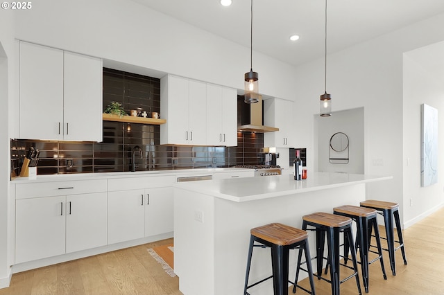 kitchen with decorative backsplash, white cabinetry, hanging light fixtures, and wall chimney range hood