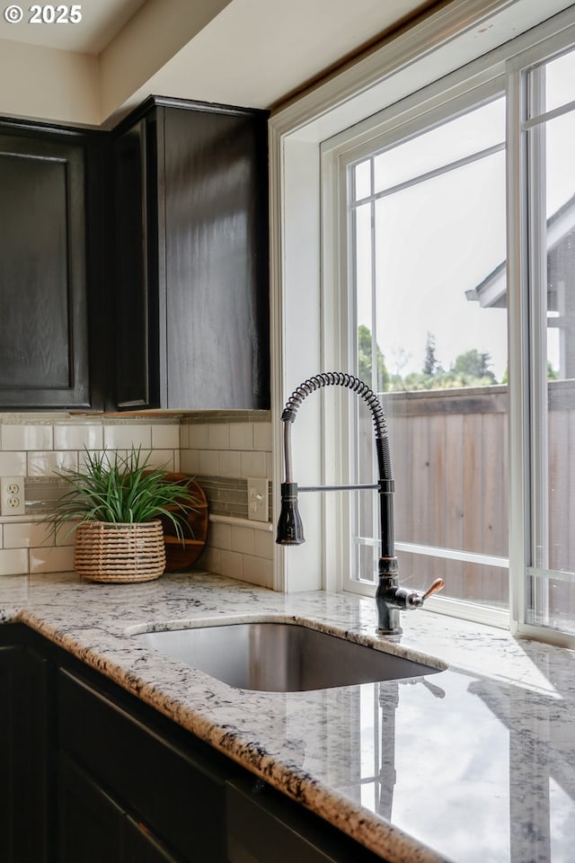 details featuring dark cabinets, a sink, decorative backsplash, and light stone countertops