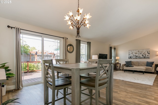 dining area with an inviting chandelier, wood finished floors, and vaulted ceiling