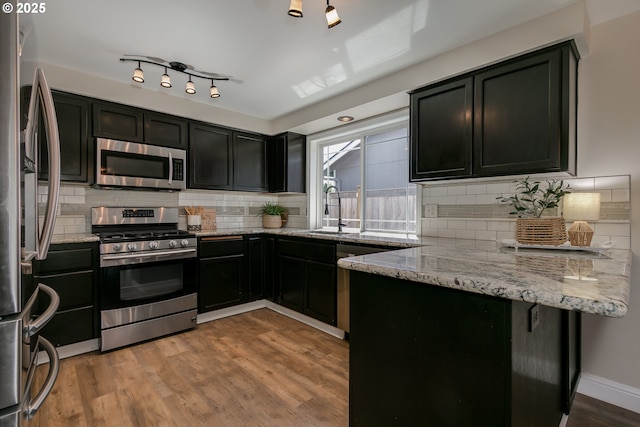 kitchen featuring light stone countertops, a sink, dark cabinetry, stainless steel appliances, and tasteful backsplash