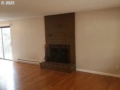 11181120 SE 45th Ave, Portland, OR 97215 - unfurnished living room with baseboard heating, wood finished floors, a fireplace, baseboards, and a textured ceiling