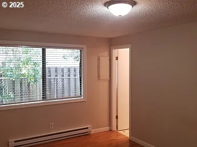 11181120 SE 45th Ave, Portland, OR 97215 - empty room featuring a baseboard radiator, a textured ceiling, wood finished floors, and baseboards