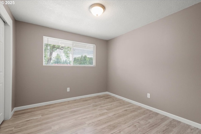 empty room featuring light wood-style floors, a textured ceiling, and baseboards