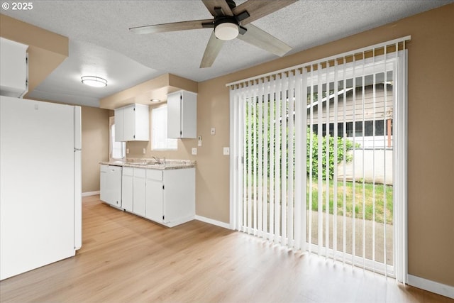 kitchen with white appliances, light wood-style flooring, baseboards, white cabinets, and a textured ceiling