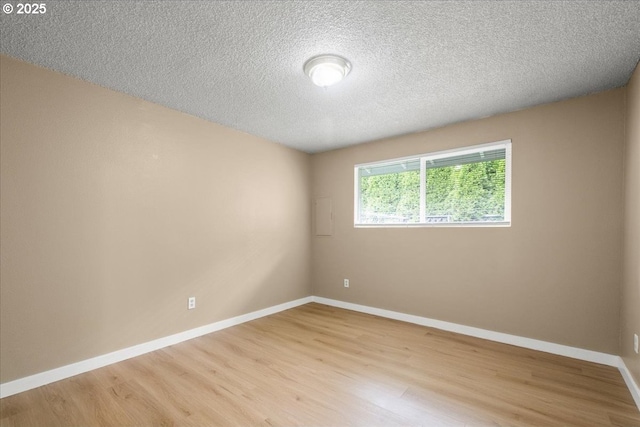spare room with light wood-style floors, baseboards, and a textured ceiling
