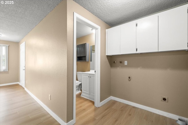 washroom featuring electric dryer hookup, cabinet space, a textured ceiling, light wood finished floors, and baseboards