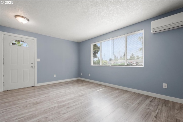 foyer entrance featuring a wall unit AC, wood finished floors, a textured ceiling, and baseboards