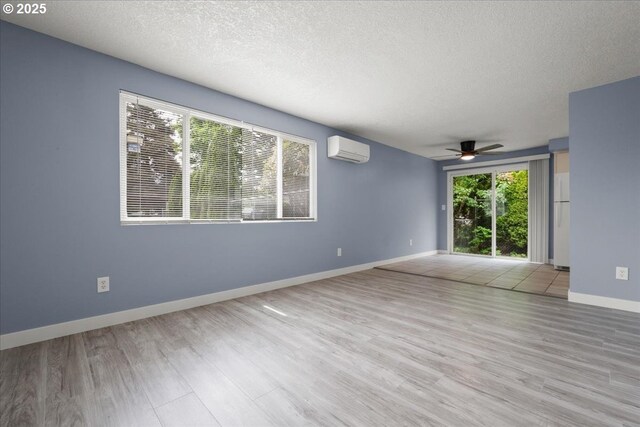 empty room featuring a wall mounted air conditioner, a textured ceiling, a ceiling fan, wood finished floors, and baseboards