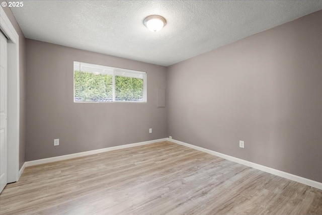 empty room featuring light wood-style flooring, a textured ceiling, and baseboards