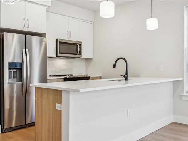 kitchen featuring hanging light fixtures, kitchen peninsula, white cabinets, and appliances with stainless steel finishes