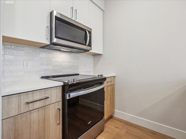 kitchen with white cabinetry, stainless steel appliances, light hardwood / wood-style floors, and decorative backsplash