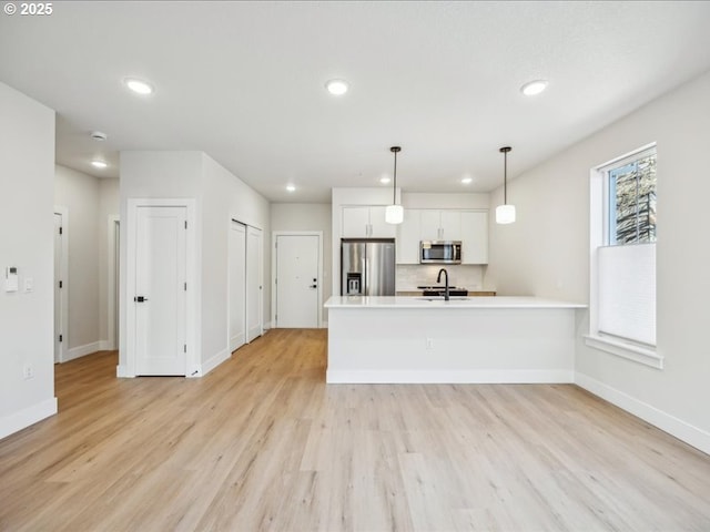 kitchen featuring sink, appliances with stainless steel finishes, light hardwood / wood-style floors, white cabinets, and decorative light fixtures