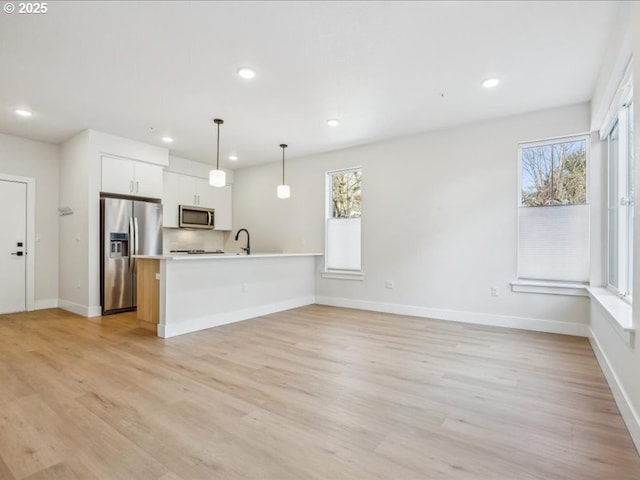 kitchen with sink, hanging light fixtures, stainless steel appliances, light hardwood / wood-style floors, and white cabinets