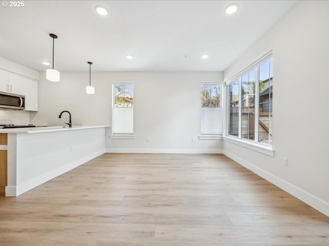 kitchen with pendant lighting, white cabinetry, a healthy amount of sunlight, and light hardwood / wood-style flooring