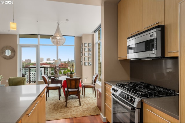 kitchen featuring stainless steel appliances, light wood-type flooring, floor to ceiling windows, hanging light fixtures, and dark countertops