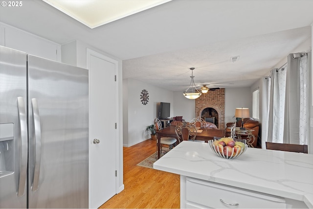 kitchen featuring a fireplace, decorative light fixtures, white cabinetry, light hardwood / wood-style floors, and stainless steel refrigerator with ice dispenser