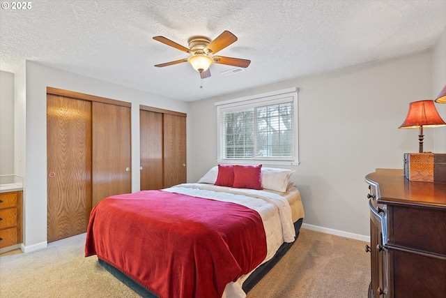 carpeted bedroom featuring ceiling fan, a textured ceiling, and multiple closets