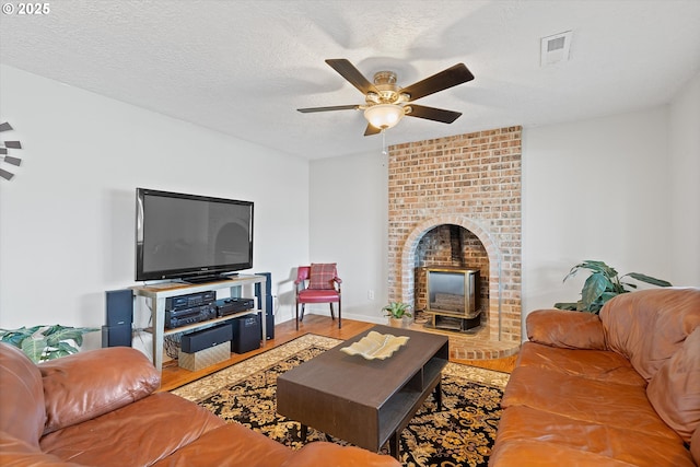 living room with ceiling fan, hardwood / wood-style floors, a textured ceiling, and a wood stove