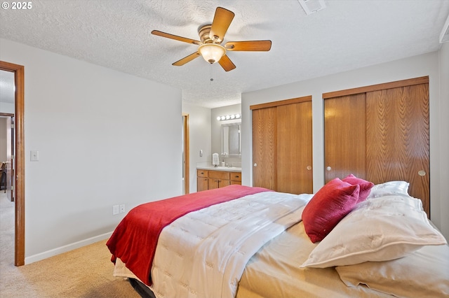 carpeted bedroom with multiple closets, ensuite bath, ceiling fan, and a textured ceiling