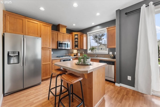 kitchen featuring sink, stainless steel appliances, a kitchen island, tile countertops, and light wood-type flooring