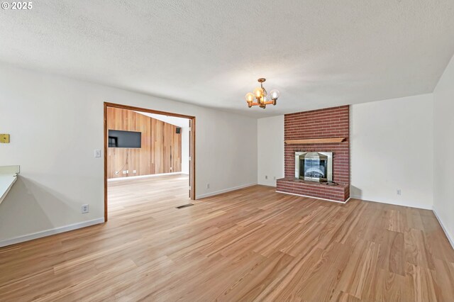 590 Granite Pl, Springfield, OR 97477 - unfurnished living room with a chandelier, light wood-style flooring, a textured ceiling, and a brick fireplace