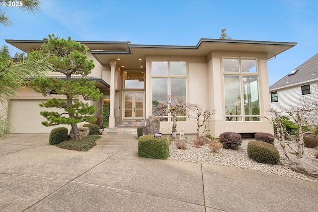 view of front of home with a garage, concrete driveway, french doors, and stucco siding