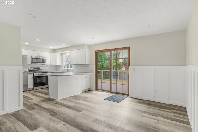 14108 NE 49th St, Vancouver, WA 98682 - kitchen with stainless steel appliances, a decorative wall, wainscoting, white cabinetry, and light wood-type flooring